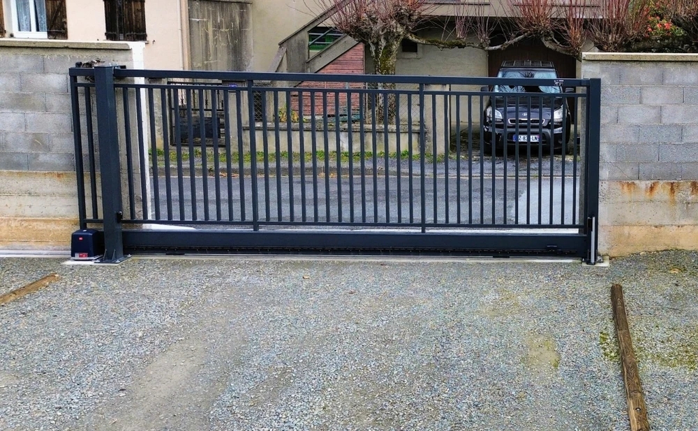 Extérieur résidentiel avec portail coulissant automatique noir en aluminium installé sur rail au sol