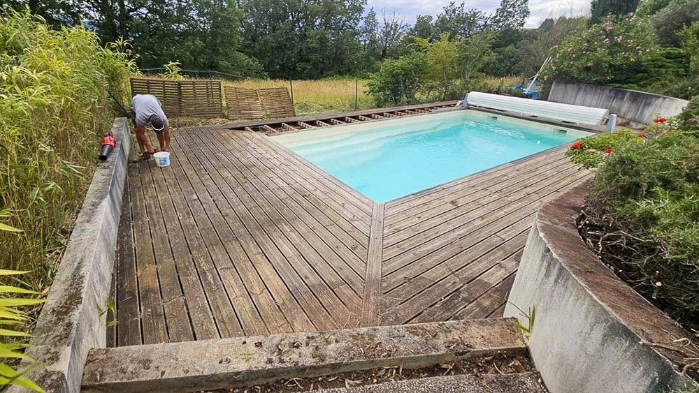 Chantier extérieur de construction terrasse piscine avec ouvrier installant lames de bois composite