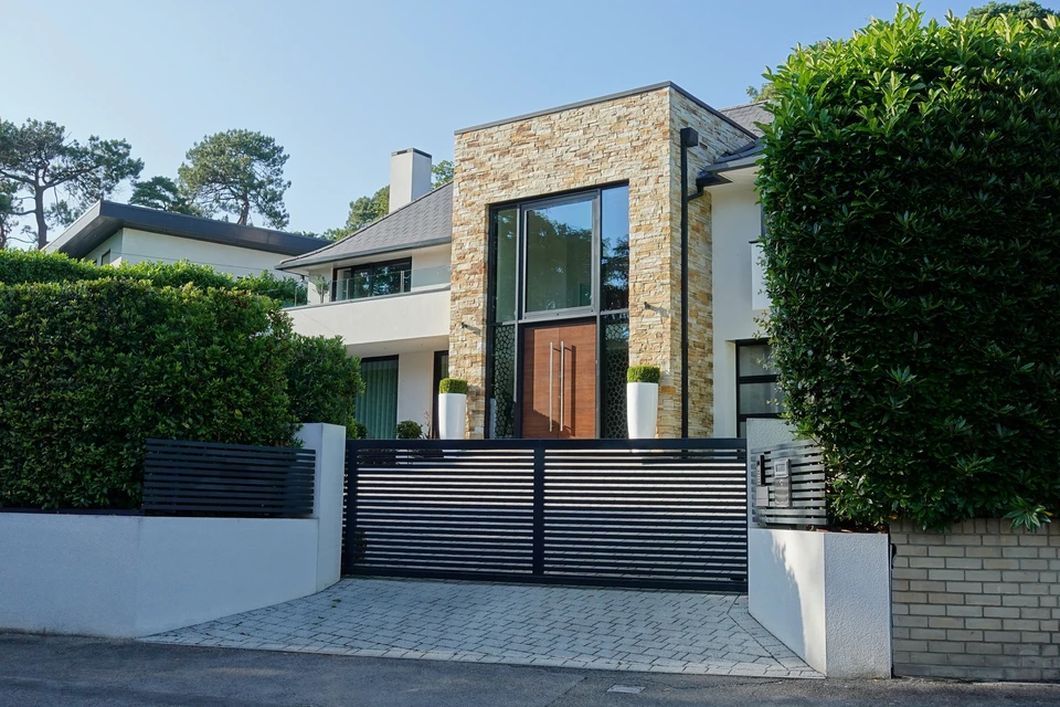 Maison moderne contemporaine avec façade en briques beiges et panneaux blancs, toit noir à deux cheminées