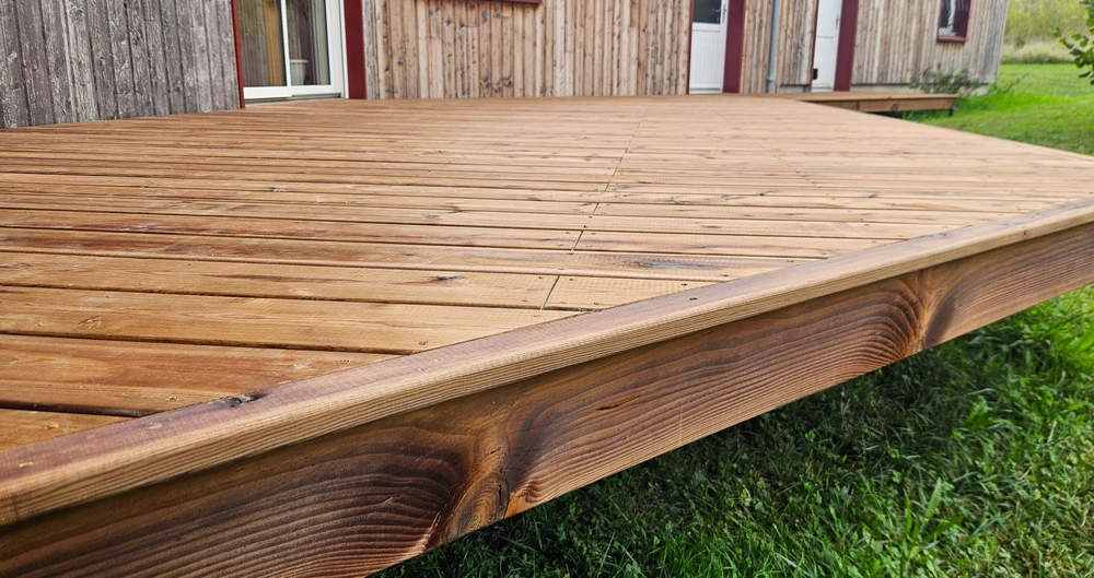 Terrasse extérieure en bois avec structure surélevée devant maison à bardage bois naturel